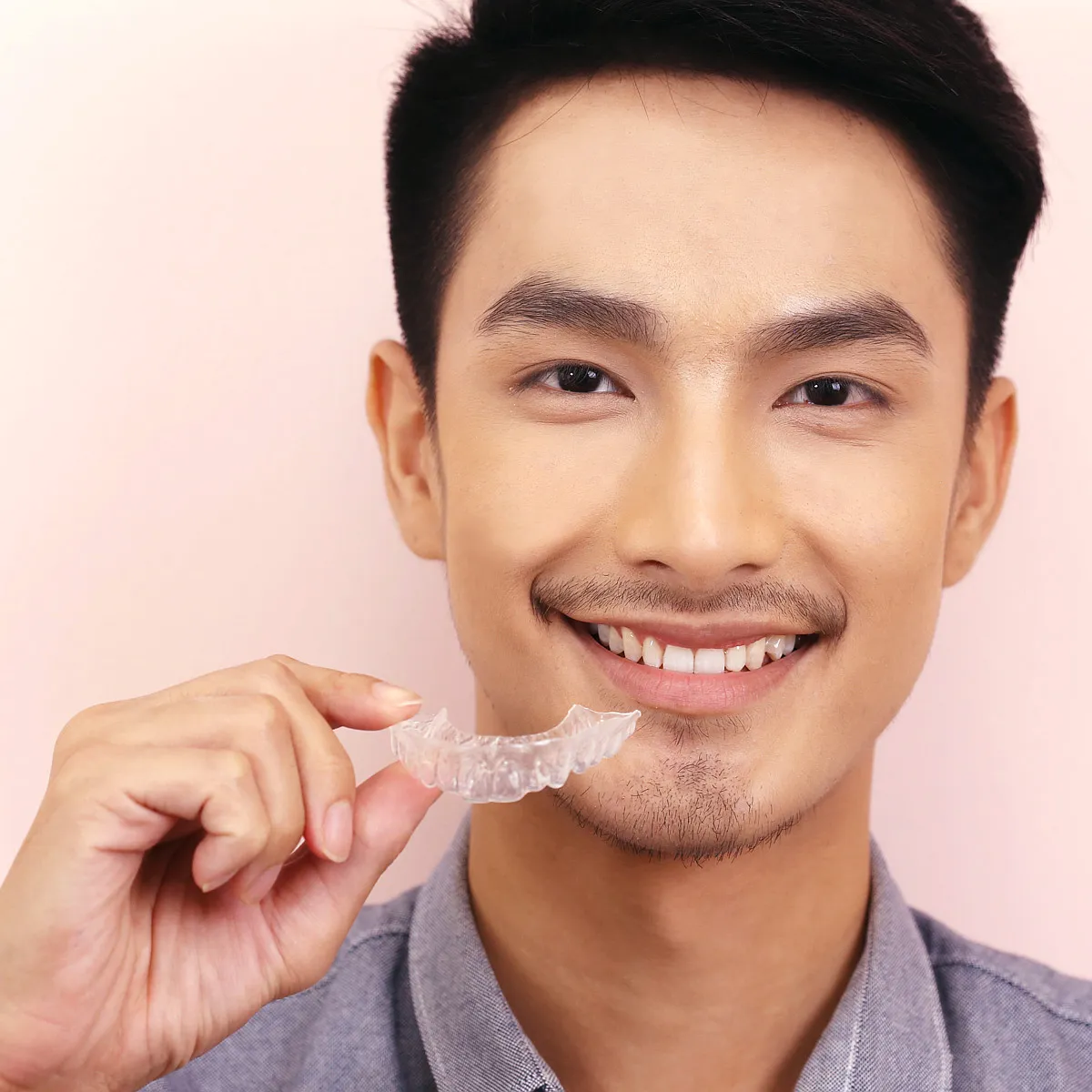 Man holding a clear aligner up to his smile