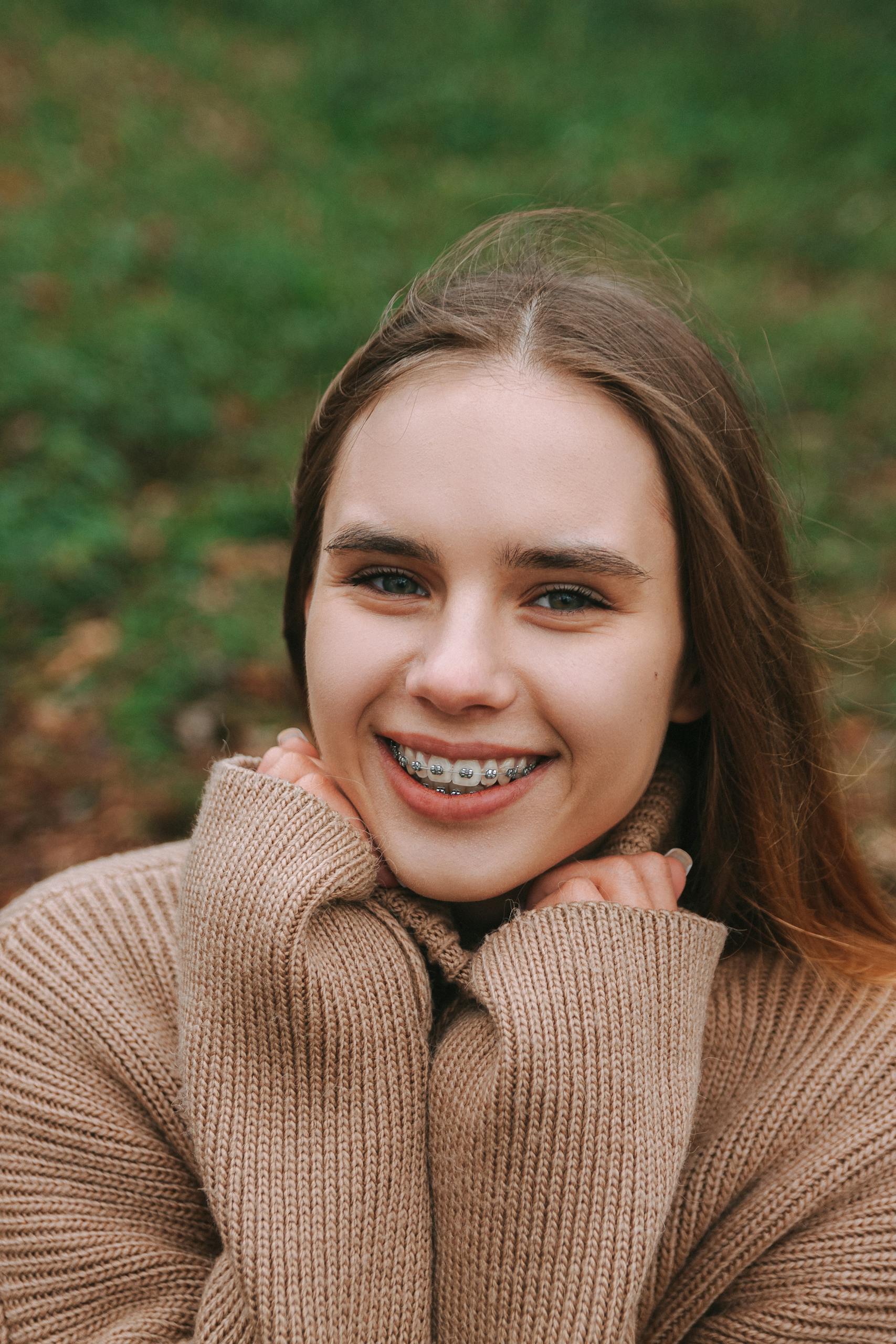 Portrait of a young woman with braces smiling outdoors in a fall setting.