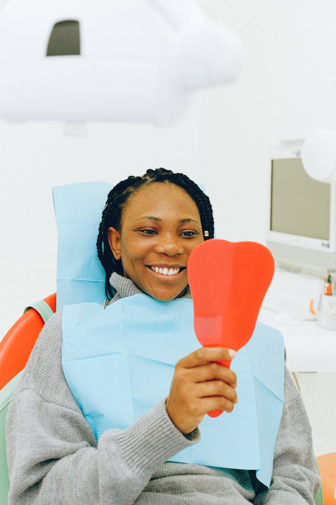 Smiling woman in a dental clinic holding a mirror, showcasing her bright smile.