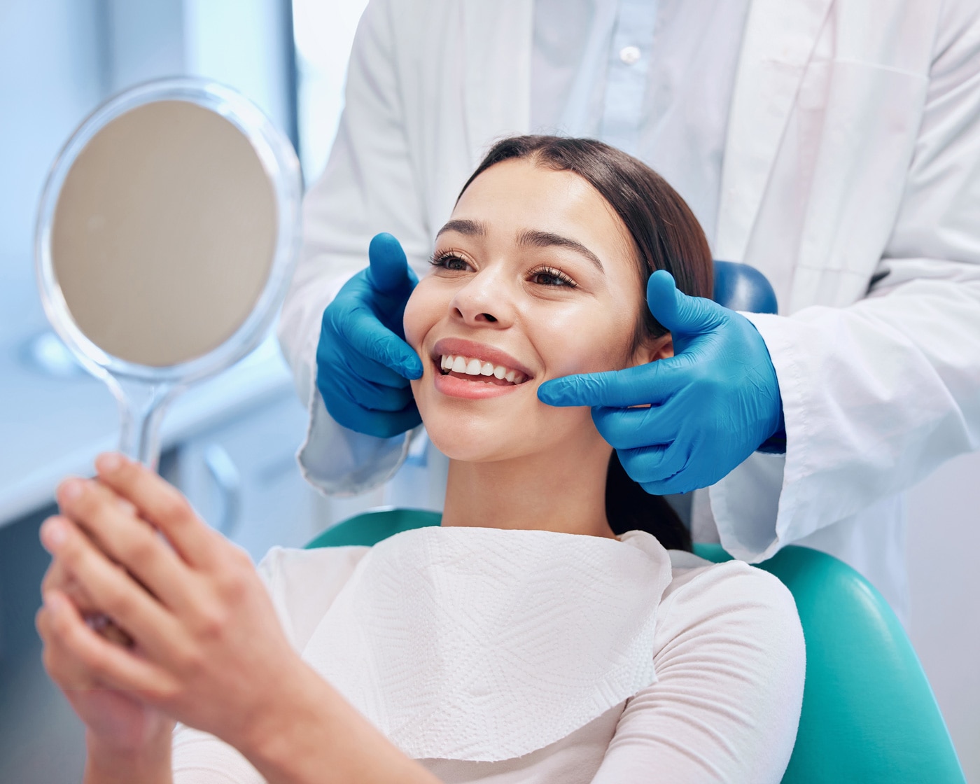 Patient smiling at her teeth in a hand mirror in the dental chair